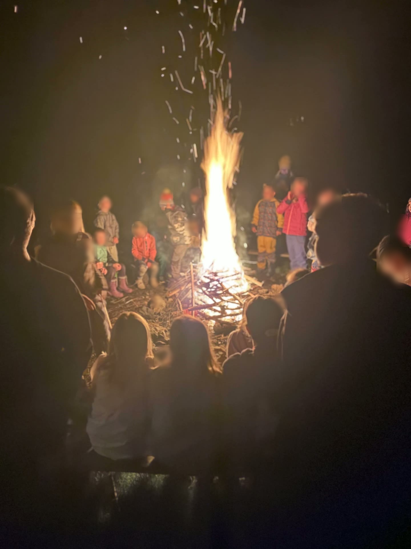 Vysoké plameny ohně a děti sledující rituál v kruhu